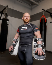 variant:black/white/grey::TITLE MMA Air Raid Thai Pads (Pair) guy holding pads down