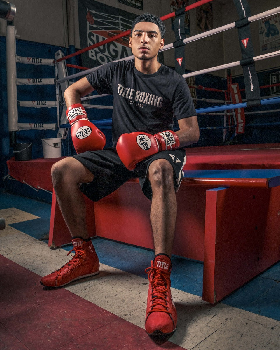 variant:Red/White::Pro Mex Professional Lace Sparring Gloves V3.0 guy sitting on bench infront of ring