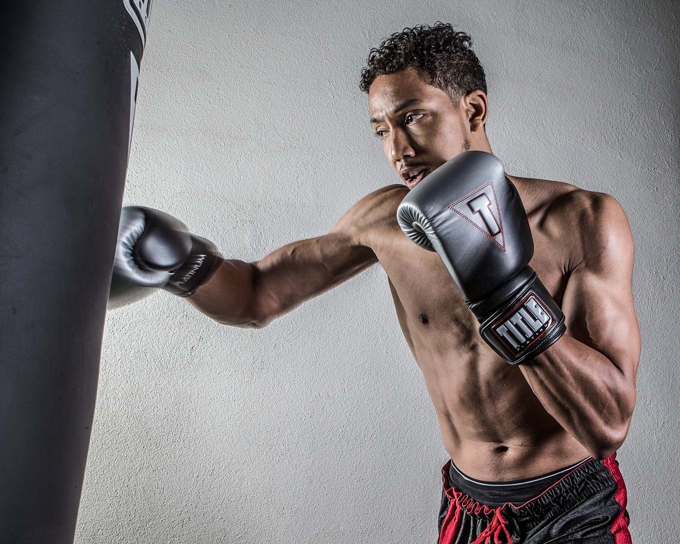 variant:lifestyle::TITLE Platinum Proclaim Power Boxing Bag Gloves guy boxing with heavy bag