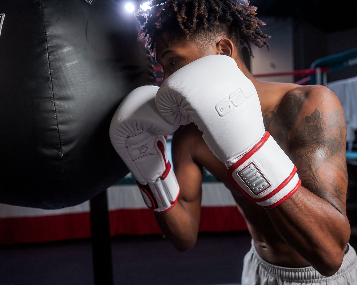 variant:lifestyle::TITLE Boxing Gel Special Edition Bag Gloves guy posing in gloves next to heavy bag