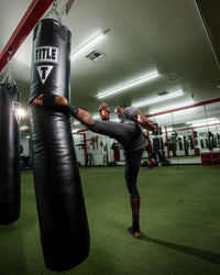 variant:lifestyle::TITLE Boxing 100lb Synthetic Thai Heavy Bag in use in a boxing gym