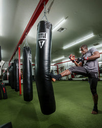 variant:lifestyle::TITLE Boxing 100lb Synthetic Thai Heavy Bag hanging in a boxing gym